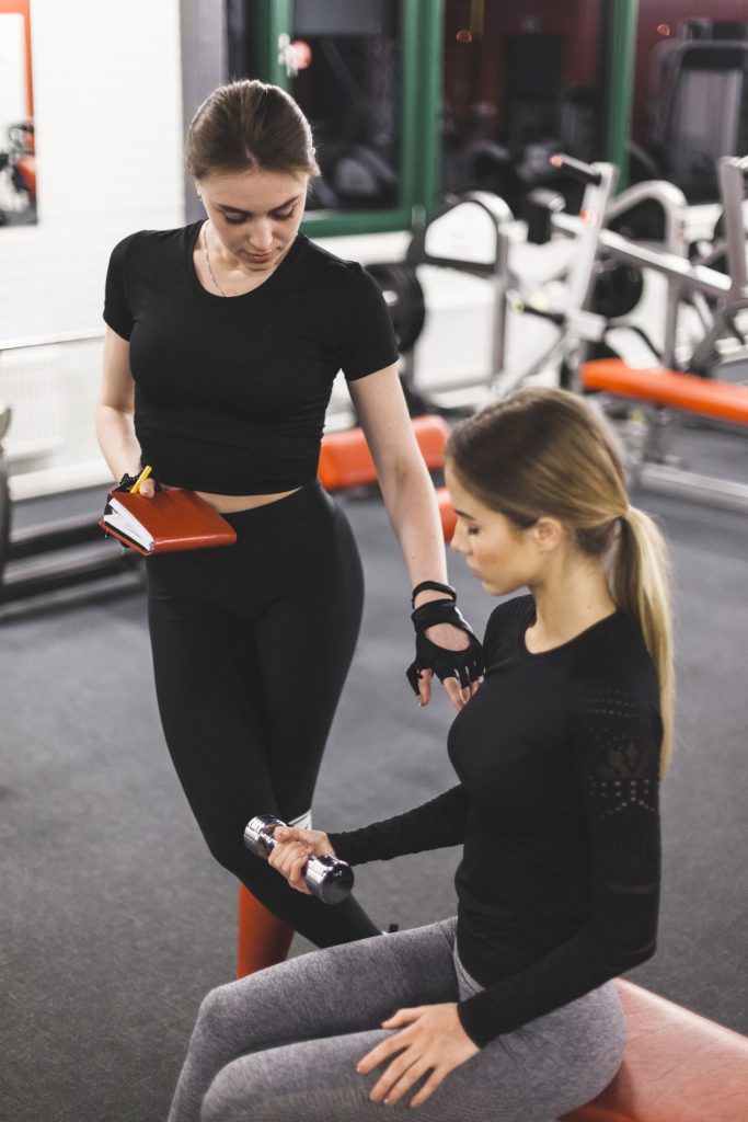 Coach ajustant la technique d'une cliente pendant une reprise de sport encadrée à Fitness Loft 78